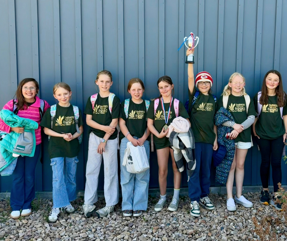 Students from the RES Battle of the Books team stand together wearing matching shirts, smiling and holding a trophy after earning second place at the UnBOCES competition.