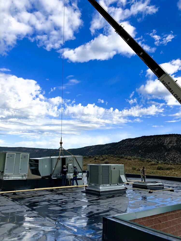 rane lifting HVAC equipment onto the roof at RSS while construction crews work under a bright blue sky.