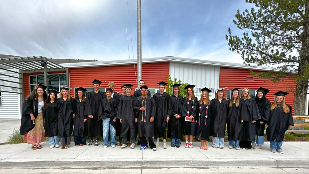 Graduating students in caps and gowns standing together outside a school building.