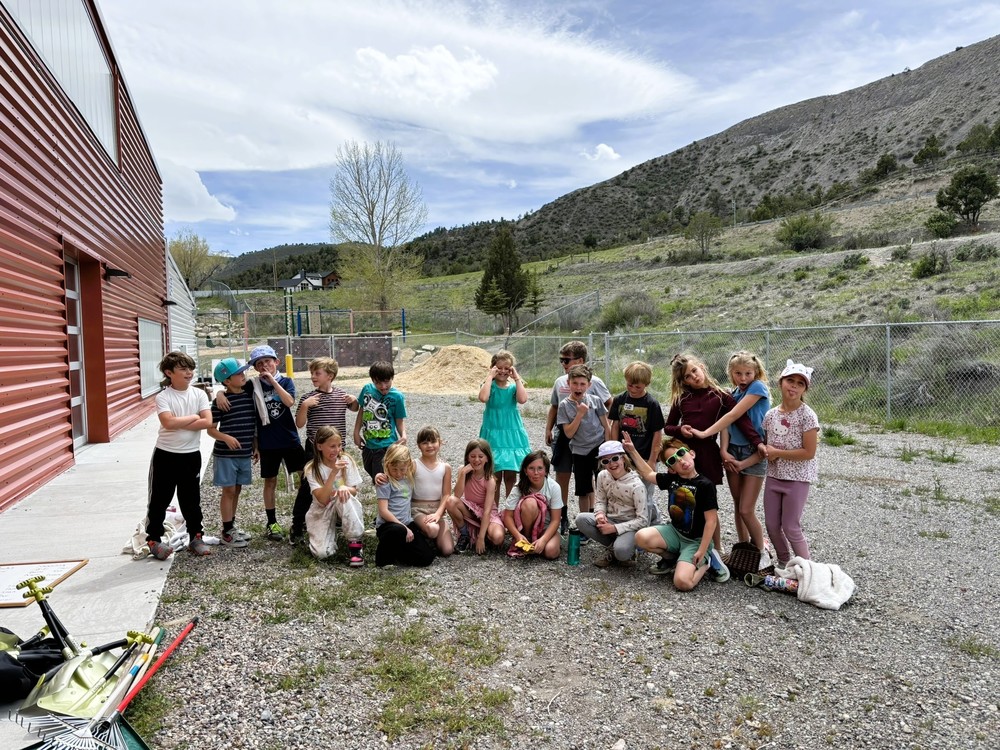 Group of students posing and making silly faces outside beside a red building, with hills and cloudy sky in the background.