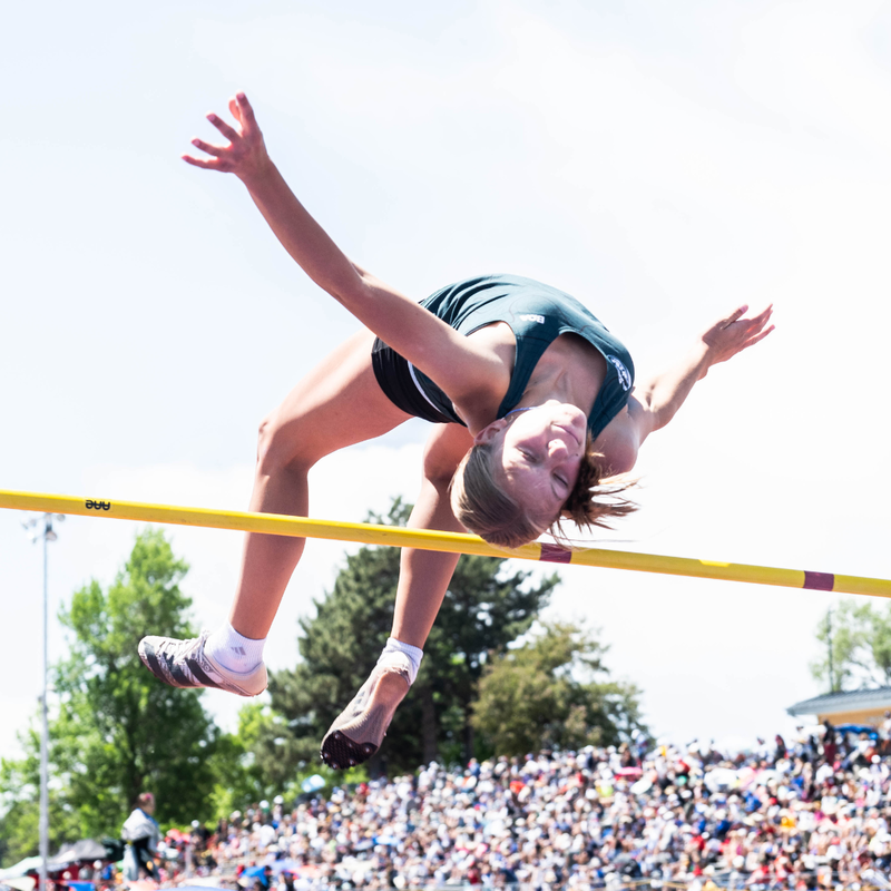 Female track athlete clearing a high jump bar during the Colorado State Track & Field Championships on a sunny day.