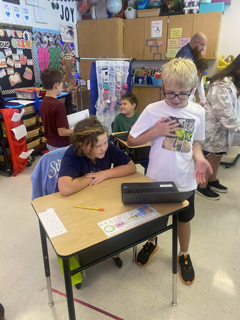 Two young children working together on a laptop. One boy is standing up.