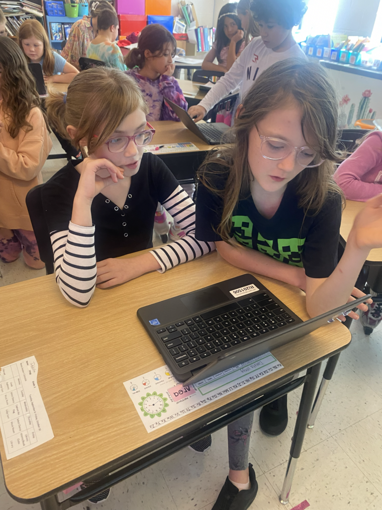 Two young girls working together on a laptop.