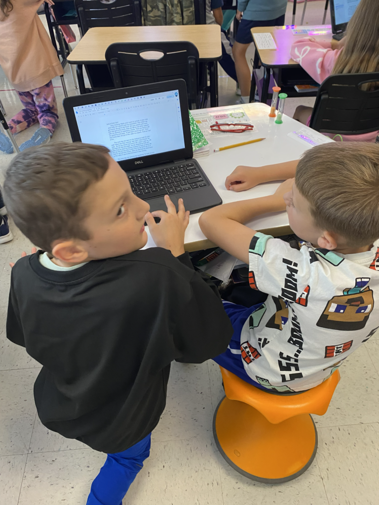 Two young children working together on a laptop.