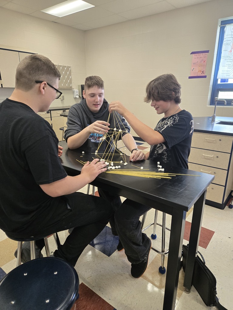 three students using triangles to make their spaghetti tower