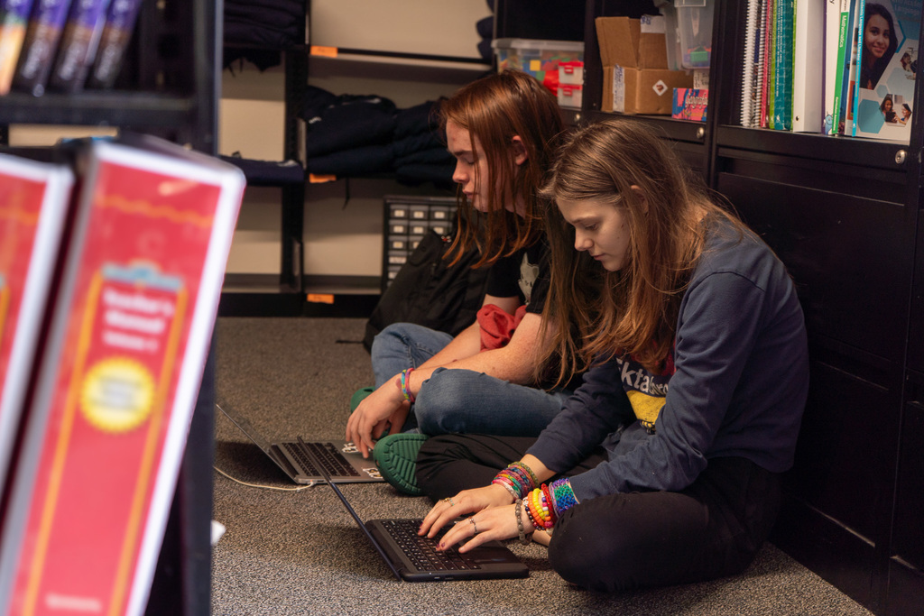 2 students sit on the floor, working on laptops