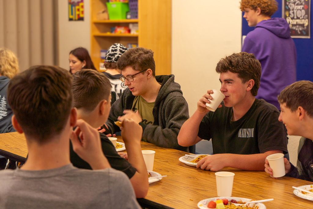 Teenage boys sit around a table, drinking water and eating lunch.
