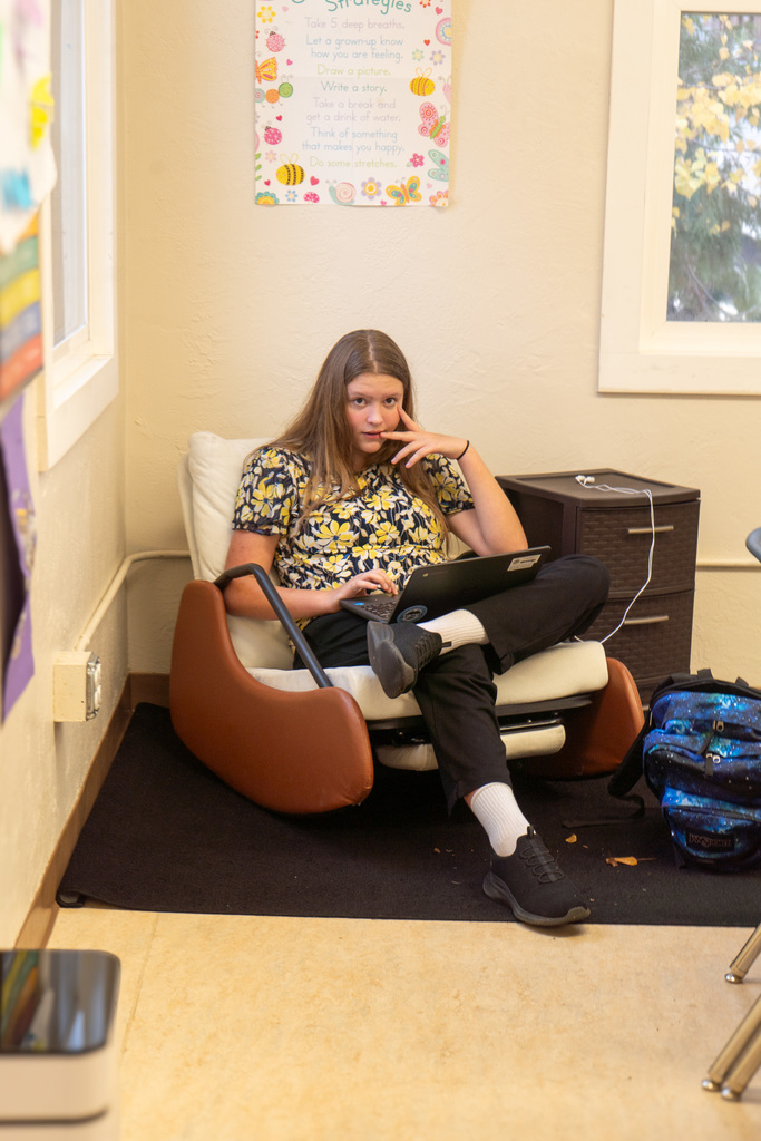 A middle school aged girl reclines in a comfortable chair with a laptop in her lap.