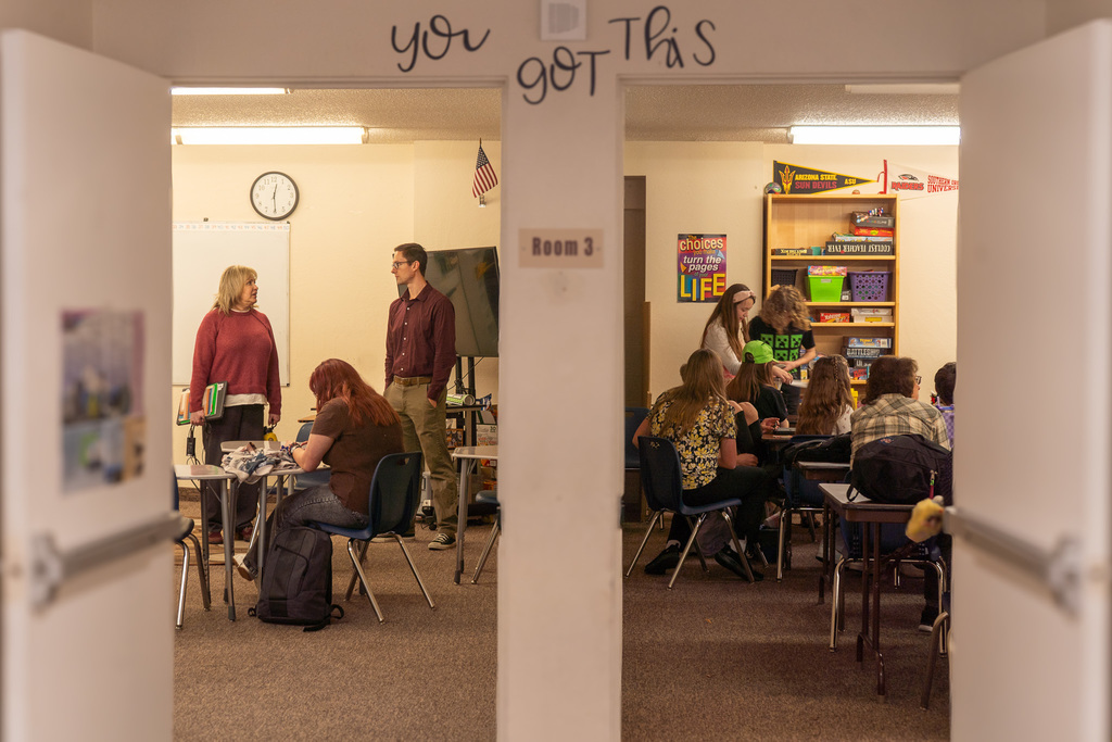A photo shows two doors: through the one the left, teachers chat while a student works. Through the one on the right, students are working together around a table. A sticker reads, "You got this," above the door. 