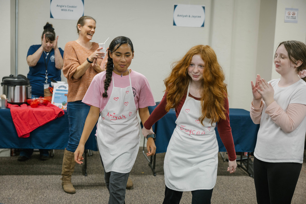 2 young girls wearing aprons hold hands as people cheer for them