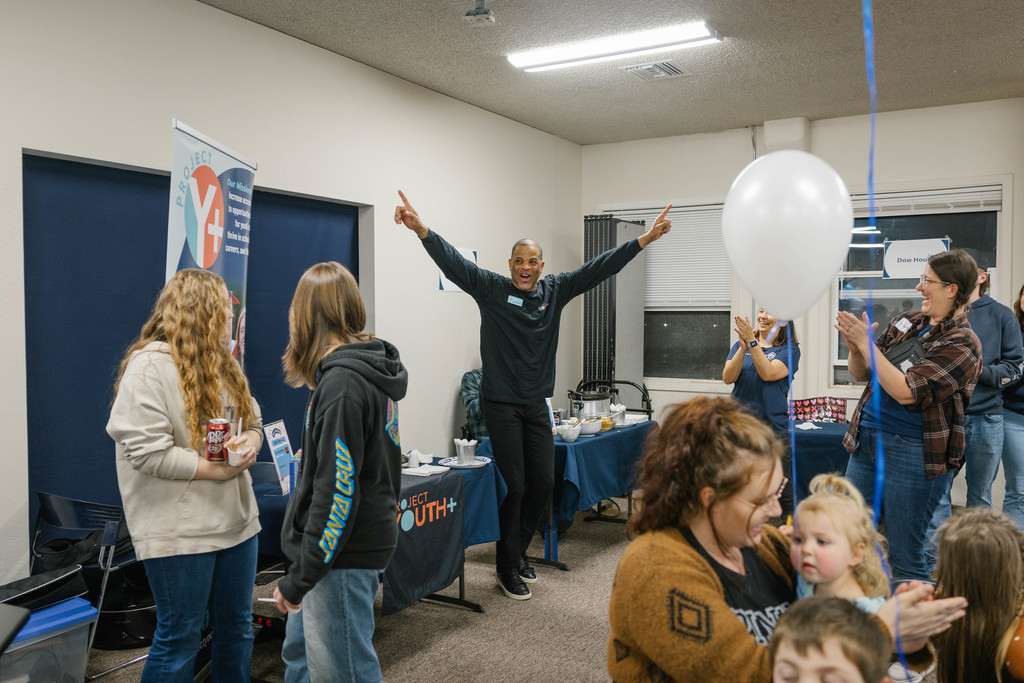 A man raises his hands in excitement in front of tables full of chili.