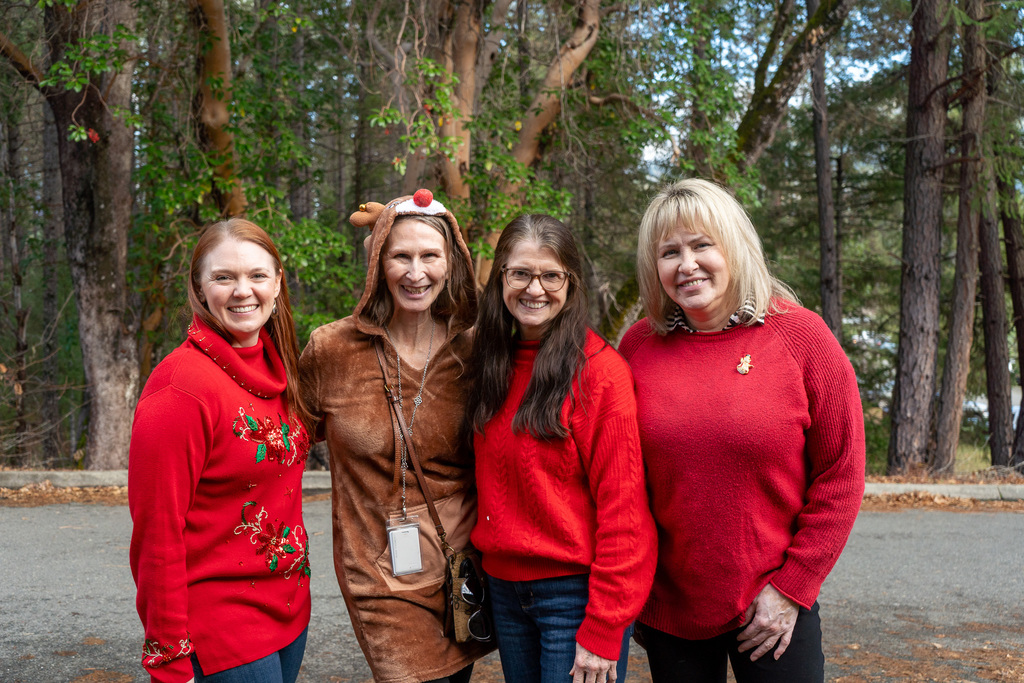 Four women dressed in festive sweaters smile