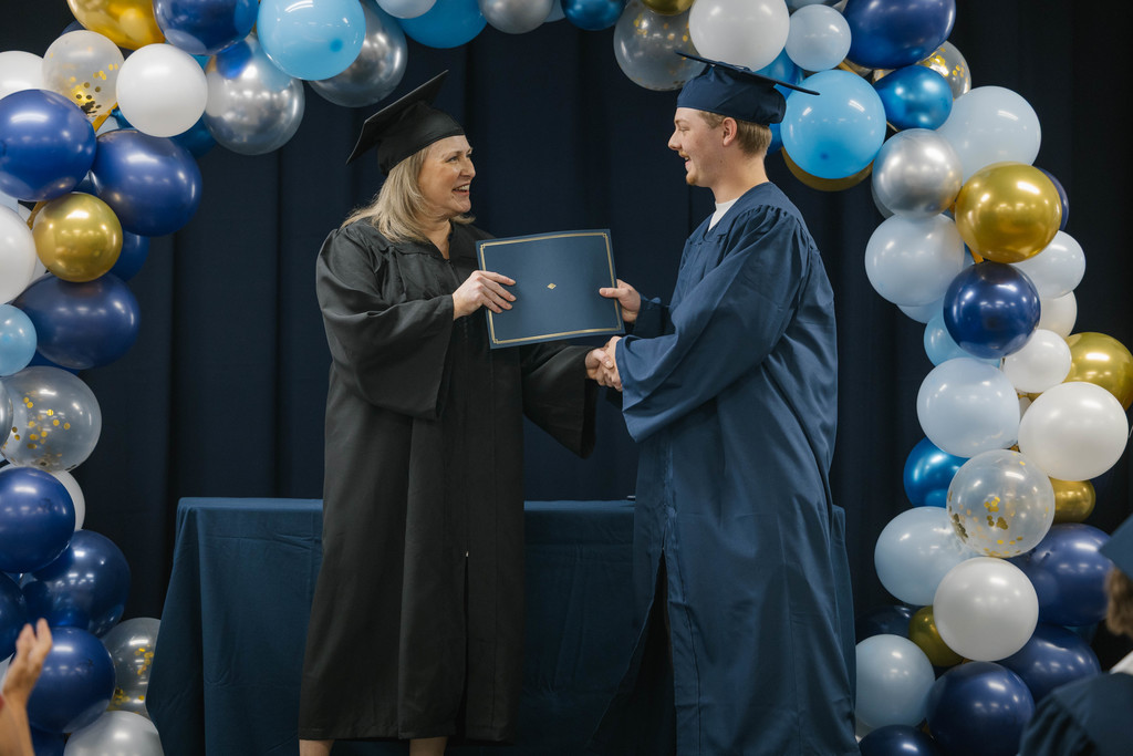 A principal hands a high school graduate a diploma and shakes his hand.