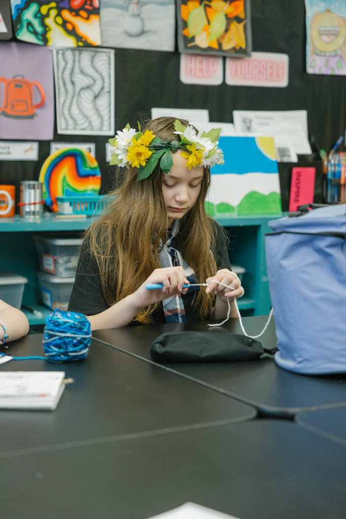 A young girl wearing a flower crown knits.