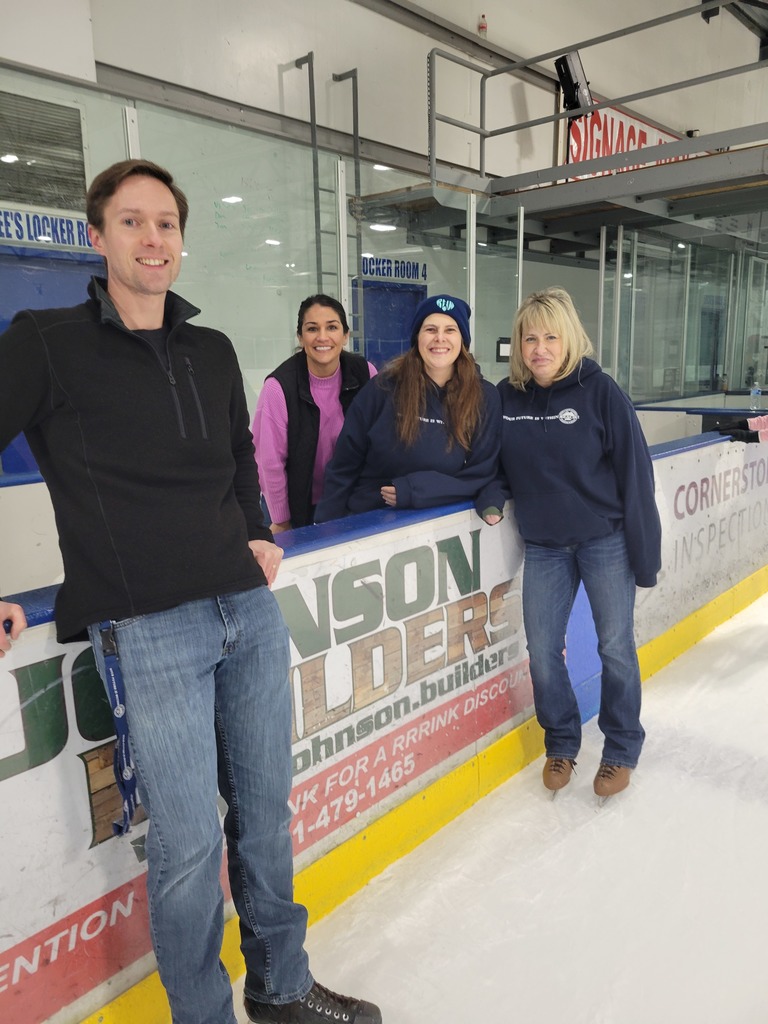 A man and three women lean against the supporting wall in an ice skating rink.