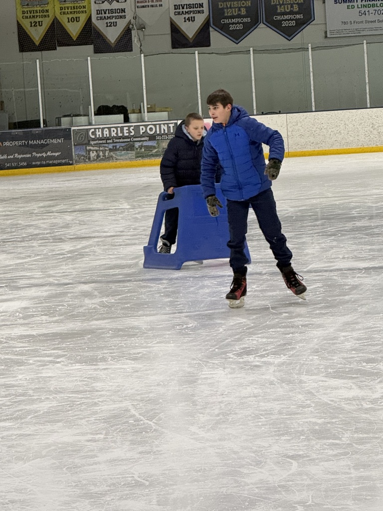 A boy in a blue jacket skates in an ice-skating rink.