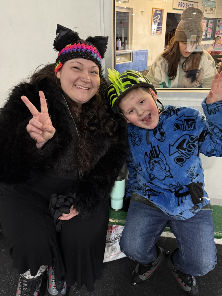 A woman wering a warm hat with fake cat ears and a young boy in a lime green helmet smile at the camera, giving the peace sign.