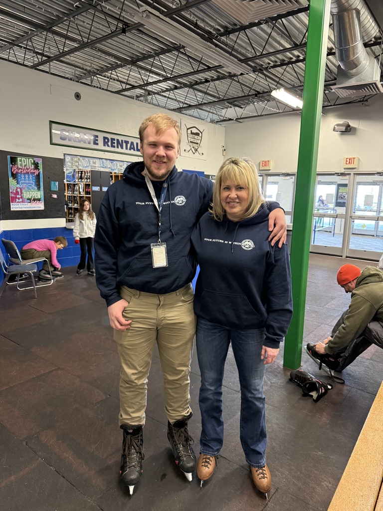 A man and a woman smile at the camera while standing on their ice skates.