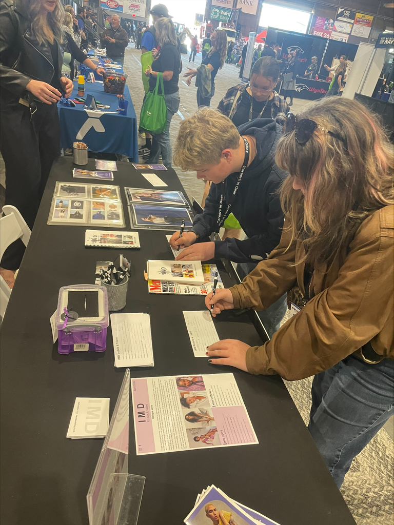 A male and a female high school student sign paperwork on a table at a career fair.