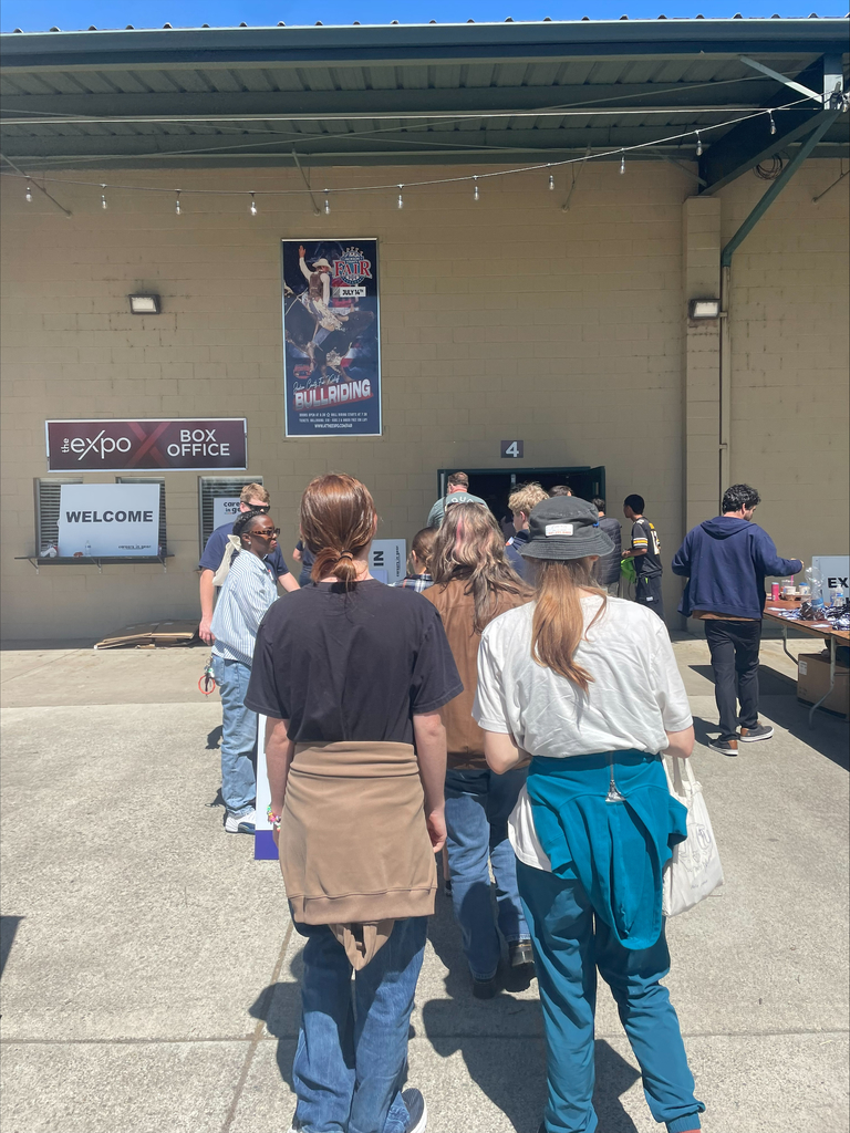 Several students stand in line outside a large building.