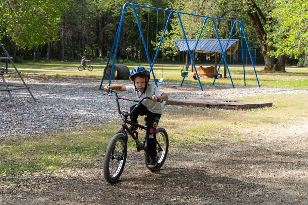 A young boy looks at the camera while riding a bike in front of a playground.