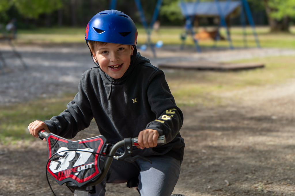 A young boy smiles at the camera while riding a bike with the number "37" on a banner on the front.