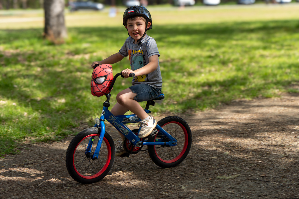 A young boy rides a Spiderman-themed bike. He smiles at the camera.