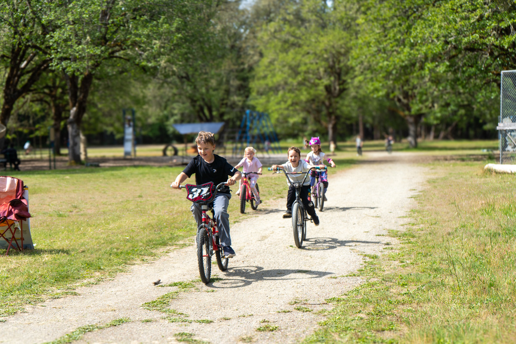 Four kids ride bikes on a track. They look excited.