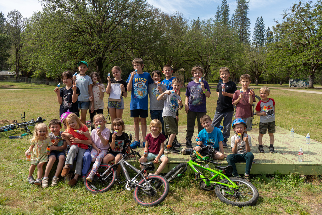 Several kids pose for a group photo with popsicles in hand. Two bikes lay on the ground in front of them.