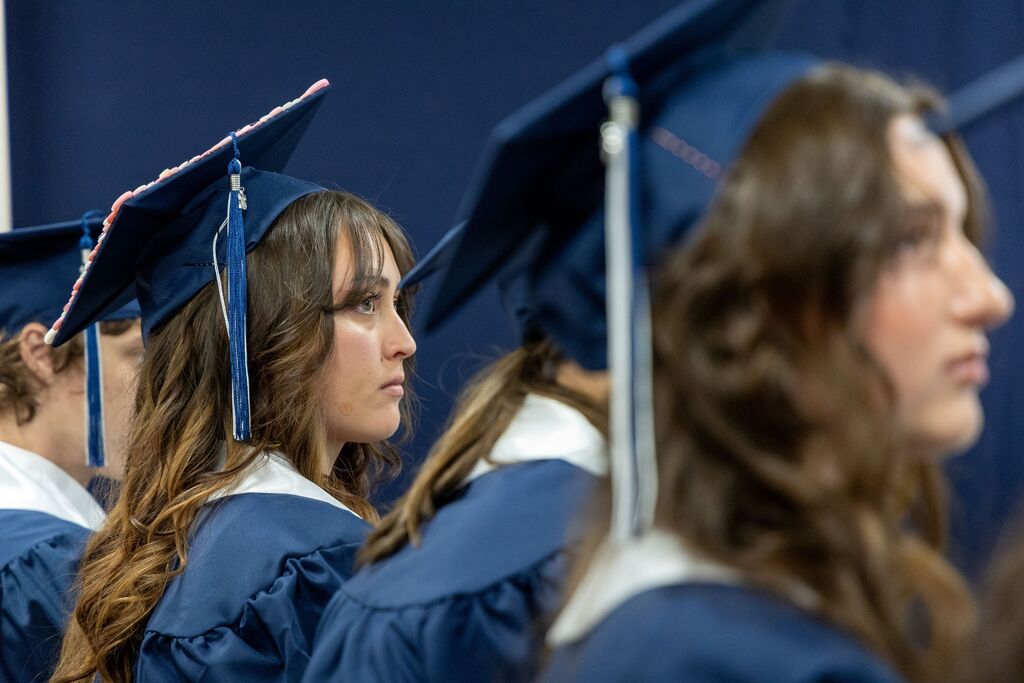 Graduation seniors in graduation regalia sit and look sincerely towards something in the distance. 