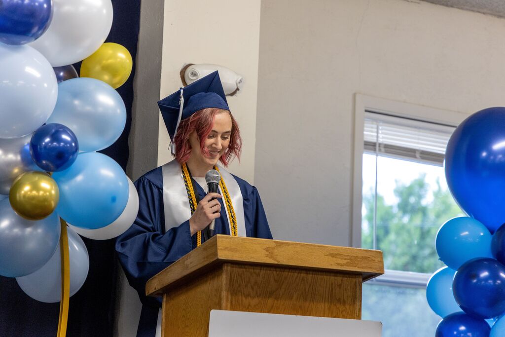 A class valedictorian in graduation regalia gives a speech from a podium. 