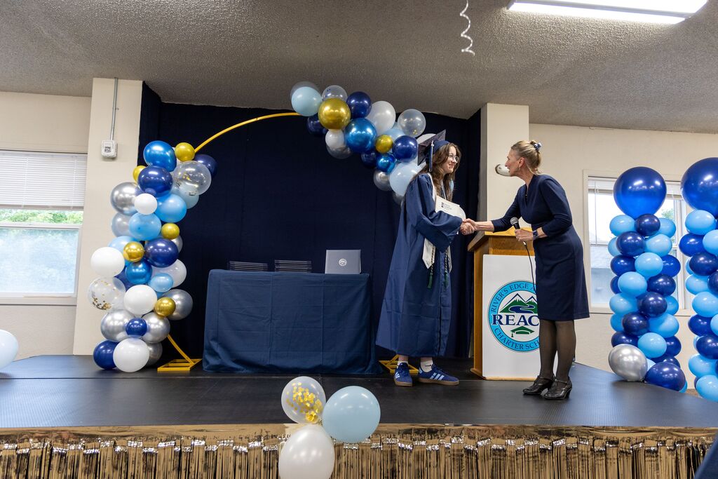 A woman shakes a graduating seniors hand and hands her a certificate. 