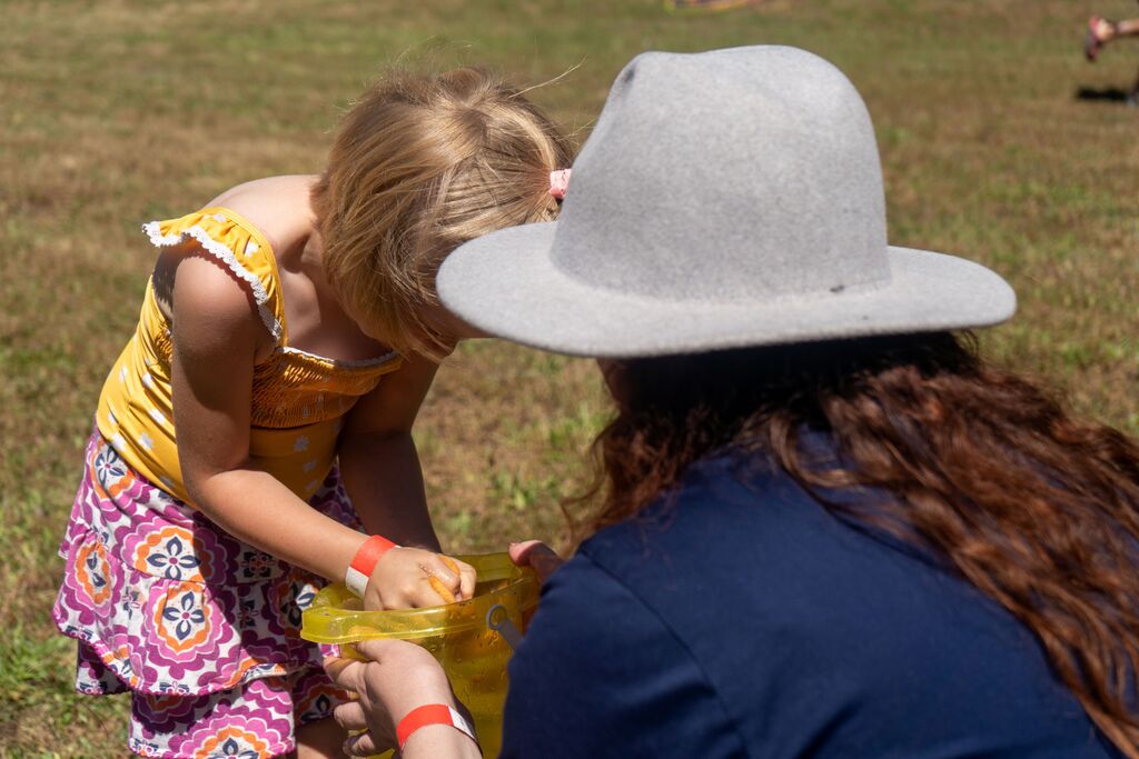 A small child squeezes a sponge into a bucket held by an adult. 