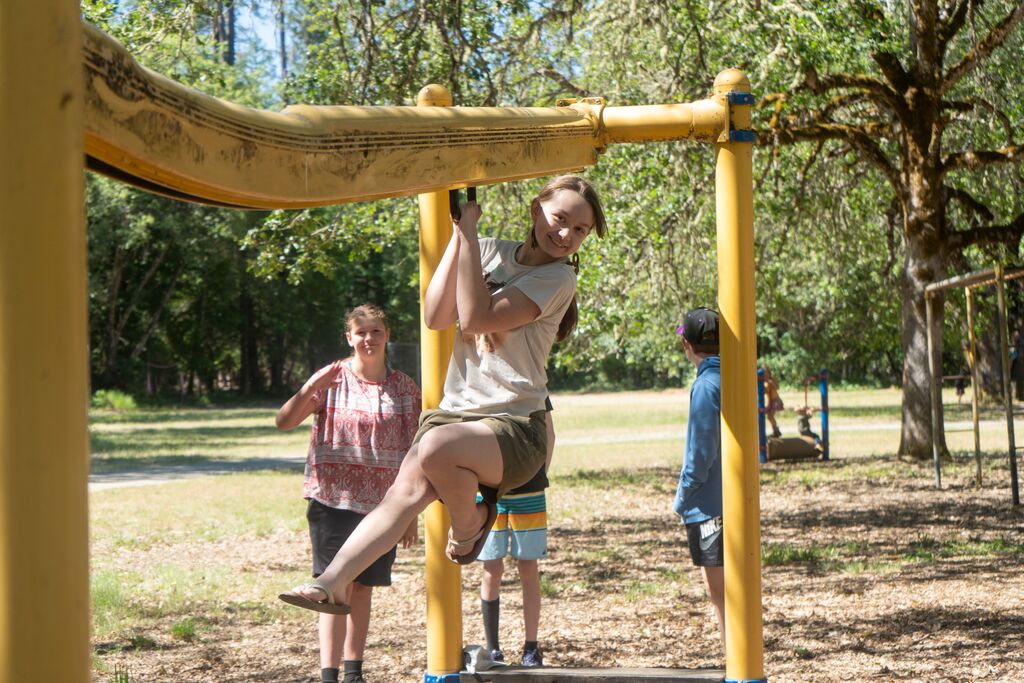 A teenager smiles at the camera as she hoists herself up some playground equipment. 