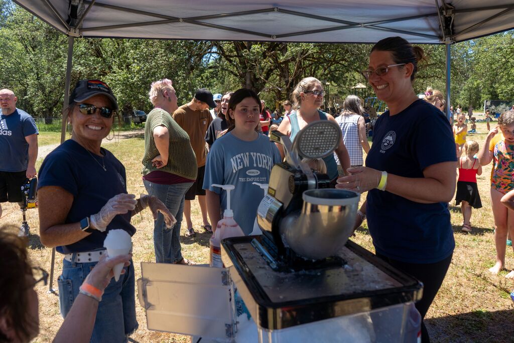 Teachers smile while making snow cones for a line of children and their family members. 