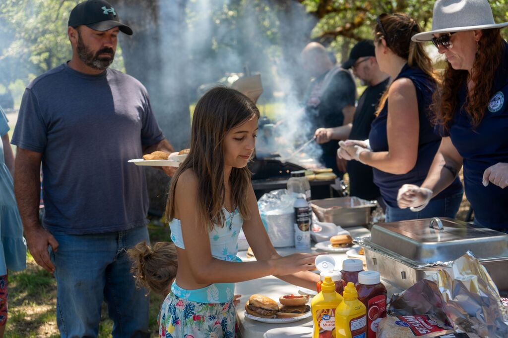 A young girl wearing a swimsuit puts ketchup on a hamburger. 