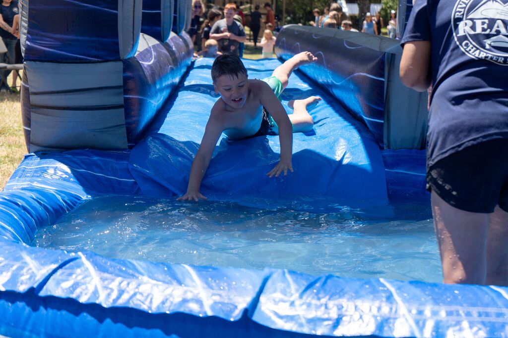 A young boy slides along an inflatable waterslide towards a pool. 