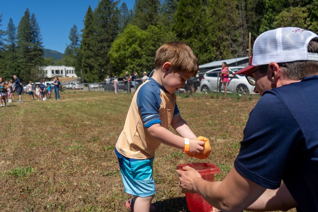 A little boy squeezes a sponge into a bucket held by an adult. 