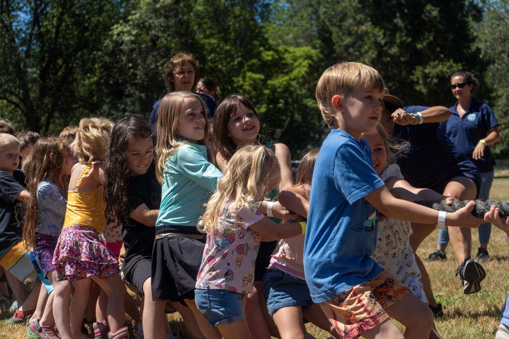 A group of small children  pull hard on one side of a rope.