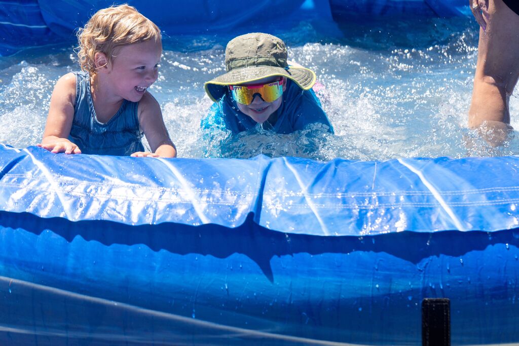 A young boy and a young girl smile in an inflatable pool. 