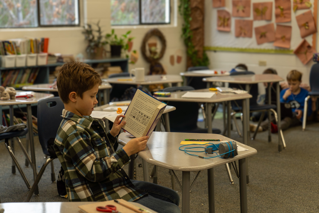 A young boy reads a book at this desk. 