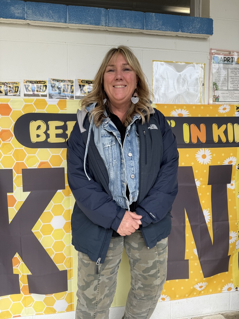 A woman smiles in front of a sign that reads, "Be the I in 'kindness'".