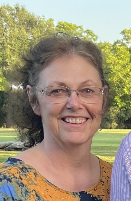 A woman with glasses smiles at the camera.