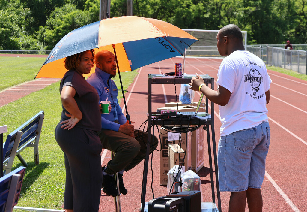Student talking to teachers under umbrella on the track
