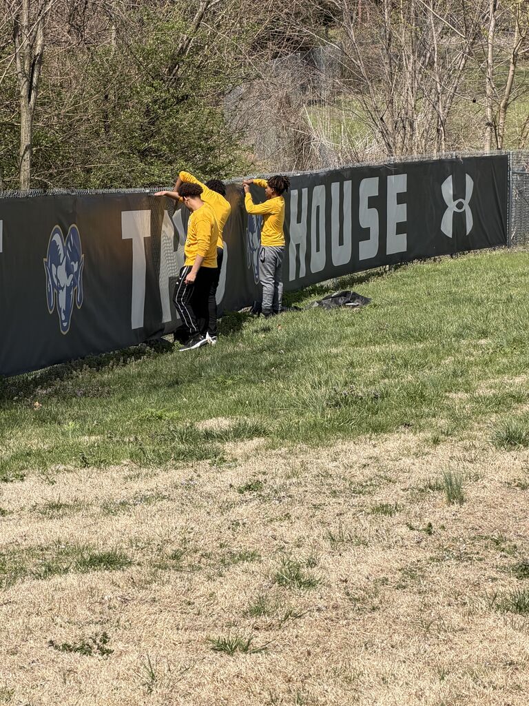 students reattach the banner on the Riverview Gardens High School baseball/softball field