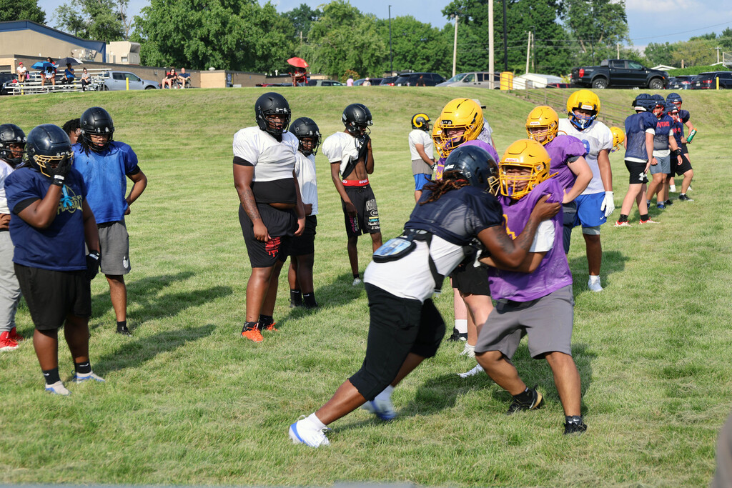 two football linemen engage each other in drill as others watch