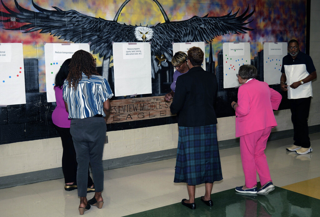 People gather around posterboards on wall and place stickers on the boards