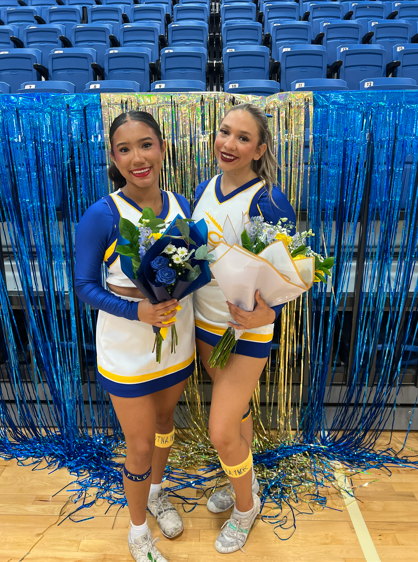 Two cheerleaders posing for a picture holding flowers. 