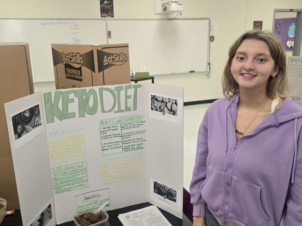 student posing with the poster and food they prepared