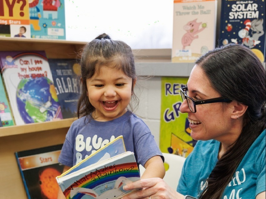 Early Childhood staff member asking questions to preschool student about a book titled "what makes a rainbow"